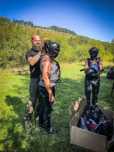 Trainer hilft Teilnehmerin beim Anlegen einer Schutzausrüstung auf einer Wiese