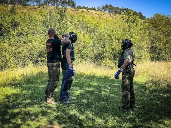 Zwei Personen in Schutzausrüstung stehen auf einer Wiese, eine wird angeleitet