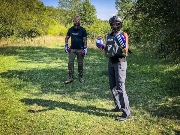 Zwei Personen in Schutzausrüstung stehen auf einer Wiese, einer bereit zum Training
