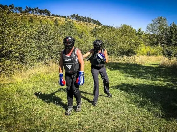 Zwei Personen in Schutzausrüstung üben Boxtechniken auf einer Wiese