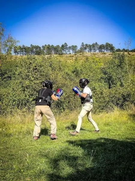 Zwei Personen in Schutzausrüstung üben Boxtechniken auf einer Wiese