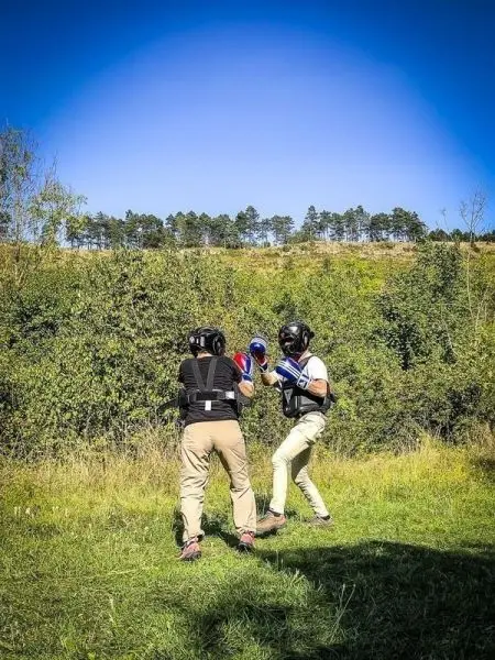 Zwei Personen in Schutzausrüstung üben Boxtechniken auf einer Wiese