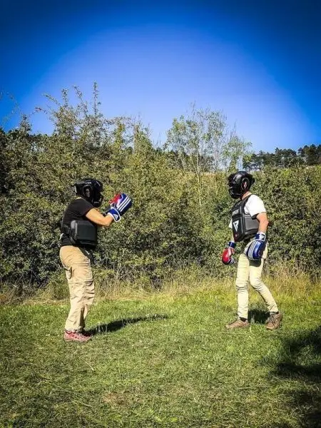 Zwei Personen in Schutzausrüstung üben Kampfsport auf einer Wiese