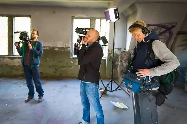 Drei Kameraleute filmen in einem leerstehenden Raum mit grauen Wänden