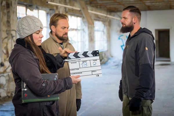 Drei Personen in einem leerstehenden Raum bereiten eine Filmszene mit einer Klappe vor