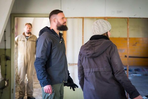Drei Personen stehen in einem leerstehenden Raum mit sichtbaren Wänden und Boden