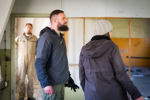 Drei Personen stehen in einem leerstehenden Raum mit sichtbaren Wänden und Boden