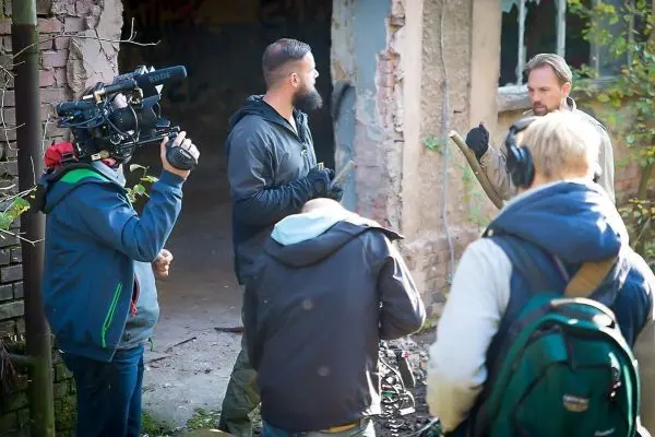 Fünf Personen stehen vor einem verfallenen Gebäude und diskutieren