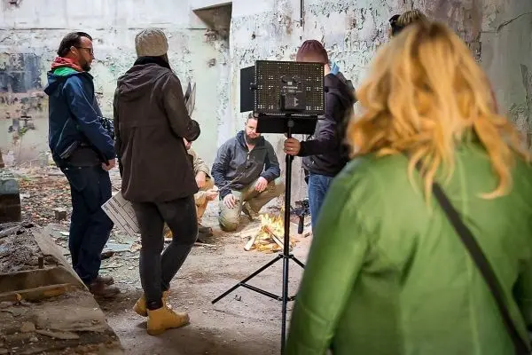 Gruppe steht um kleines Bodenfeuer in leerem Raum mit abblätternder Farbe