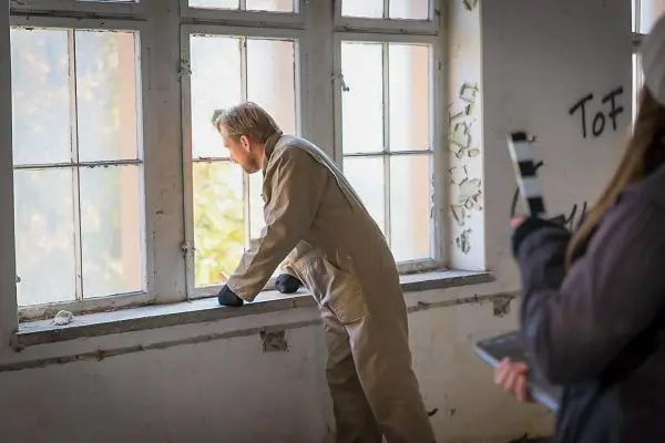 Mann in Arbeitskleidung lehnt sich an ein Fenster in einem verlassenen Raum