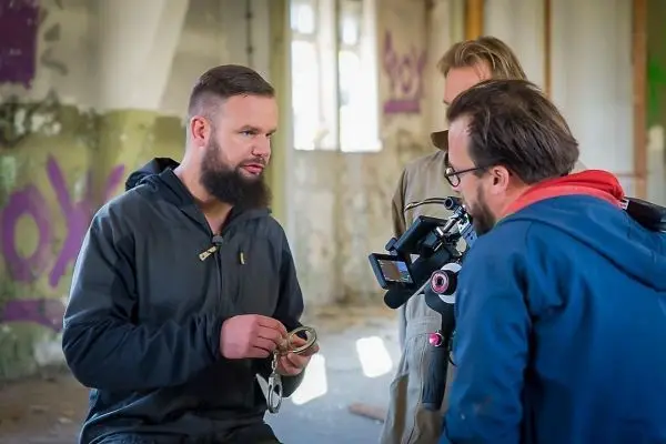 Mann zeigt Ausrüstung während Interview in leerem Raum