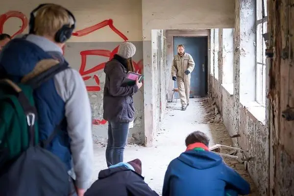Personen stehen in einem verfallenen Raum, eine Person beobachtet einen anderen