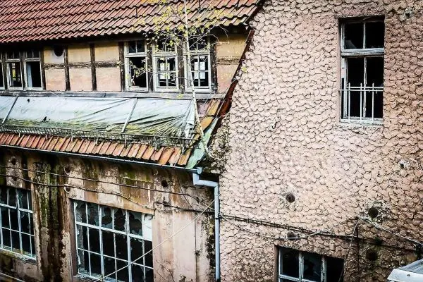 Verfallenes Gebäude mit beschädigten Fenstern und bewachsenem Dach