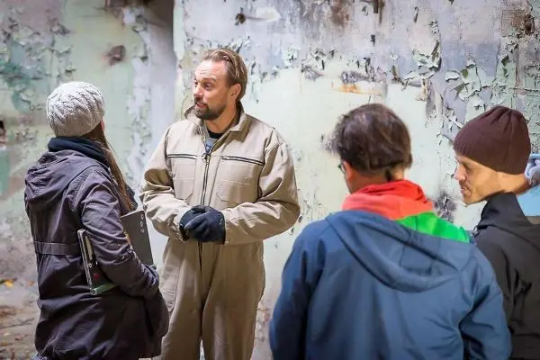 Vier Personen stehen in einem Raum mit abblätternder Farbe und diskutieren