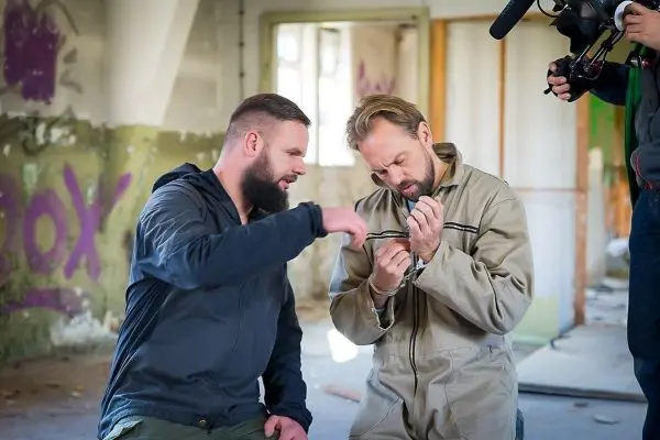 Zwei Männer in einem Raum, einer zeigt auf ein Handfesselschloss