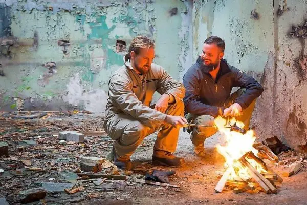 Zwei Personen sitzen vor einem Feuer und fügen Holz hinzu