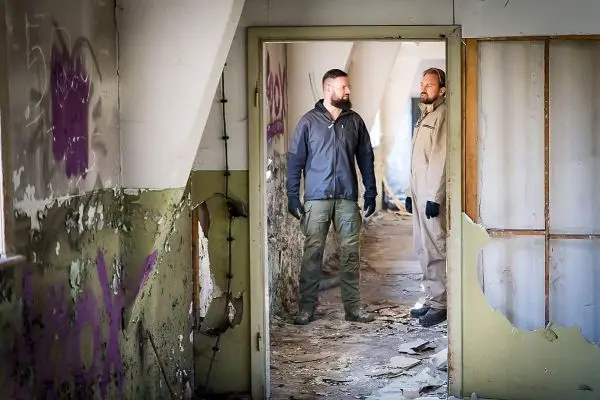 Zwei Personen stehen im Türrahmen eines verfallenen Raumes mit Graffiti