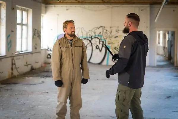 Zwei Personen stehen in einem leerstehenden Raum mit Graffiti und diskutieren