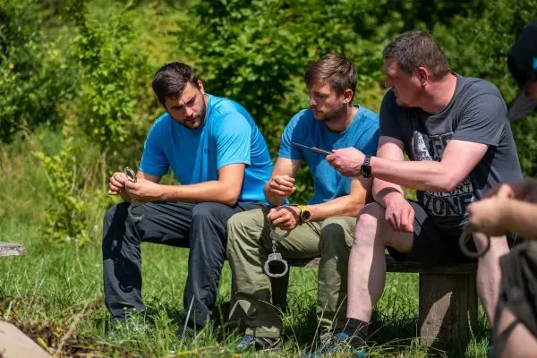 Drei Personen sitzen auf einer Bank und diskutieren über eine Handfessel