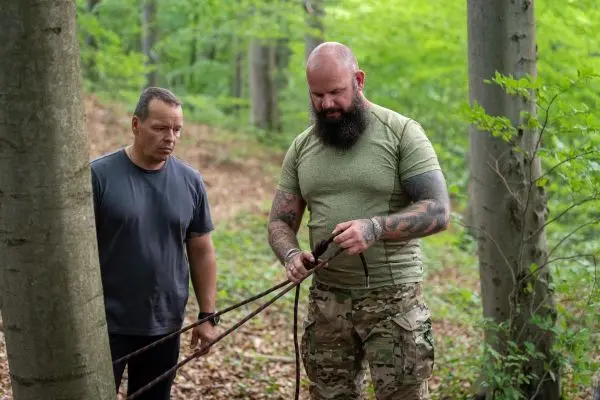 Ein Mann bindet ein Seil um einen Baumstamm, während ein anderer zuschaut