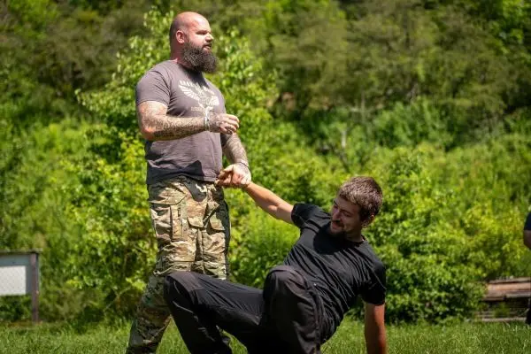 Ein Mann zieht einen anderen am Arm, während dieser auf dem Boden sitzt