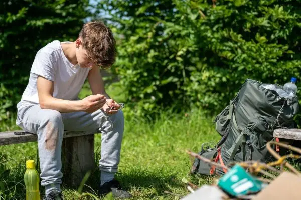 Ein Rucksack steht neben einer Holzbank, während eine Person mit einem Messer arbeitet
