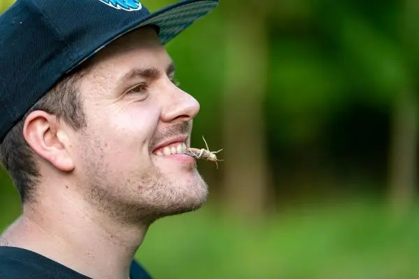 Grashüpfer hängt an Lippen eines lächelnden Mannes im Freien