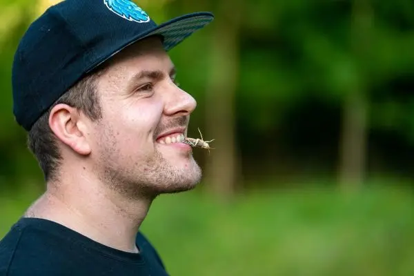 Grashüpfer sitzt auf der Lippe eines lächelnden Mannes im Freien