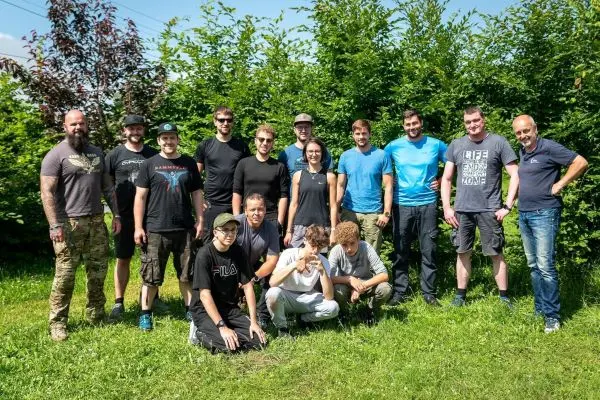 Gruppierung von Personen im Freien vor einer Hecke, einige knien, andere stehen
