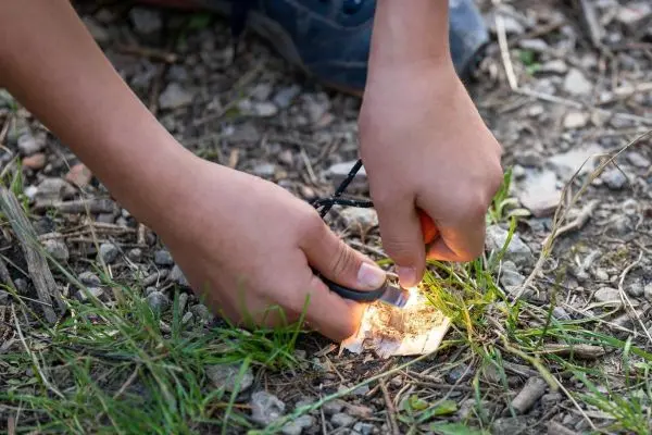 Hände entzünden Papier mit Feuerstahl auf dem Boden beim Überlebenstraining