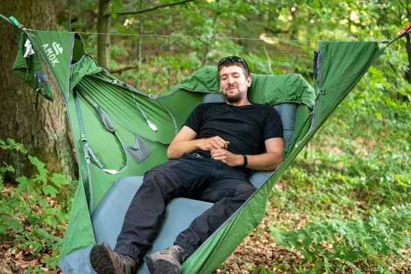Hängematte ist zwischen Bäumen gespannt, Person liegt entspannt darin