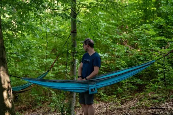 Hängematte zwischen Bäumen gespannt, Person steht daneben und schaut nachdenklich