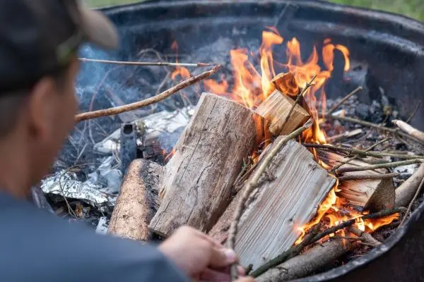 Holz wird in ein Feuer gelegt, das in einer Feuerschale brennt