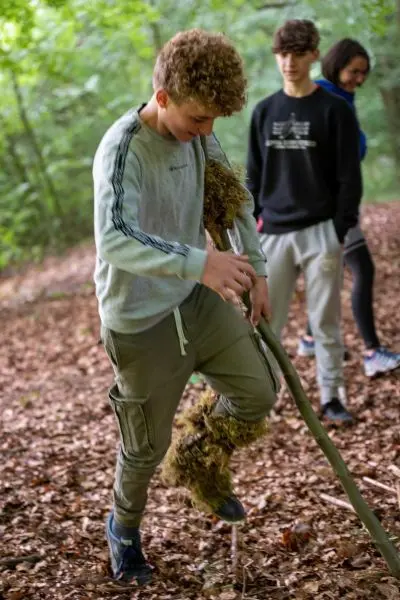 Junge hebt einen Stock mit Moos im Wald an