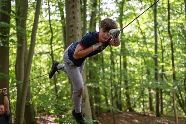 Junge schwingt an einem Seil zwischen Bäumen im Wald