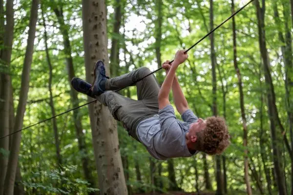Junge schwingt an einer Seilbrücke zwischen Bäumen im Wald