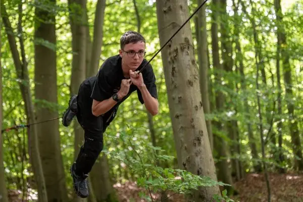 Junge schwingt an einer Seilbrücke zwischen Bäumen im Wald