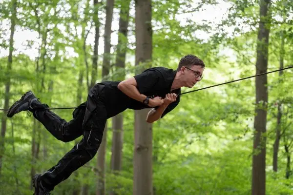 Junge schwingt an einer Seilbrücke zwischen Bäumen im Wald