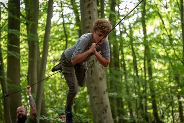 Junge überquert selbstgebaute Seilbrücke zwischen Bäumen im Wald