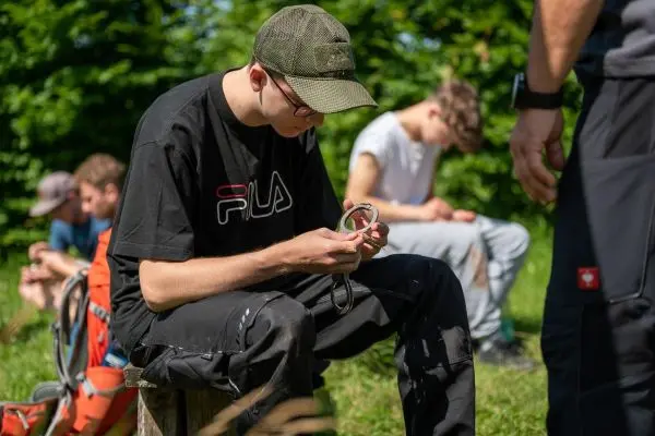 Junger Mann knotet Paracord auf einer Holzbank im Freien