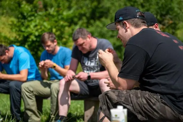 Männer bearbeiten Holzstücke mit Messern auf Holzbank im Freien