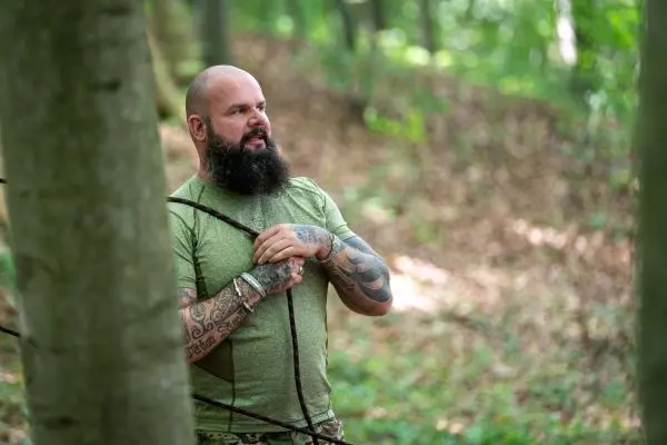 Mann hält zwei Seile in der Hand und steht zwischen Bäumen im Wald