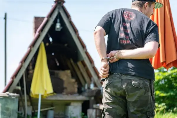 Mann mit Handschellen hinter dem Rücken steht vor einer Holzkonstruktion