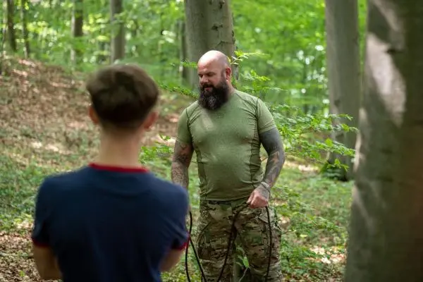 Mann mit Seil steht im Wald und erklärt einem Jugendlichen eine Technik