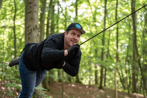 Mann nutzt Seil für eine selbstgebaute Seilbrücke im Wald
