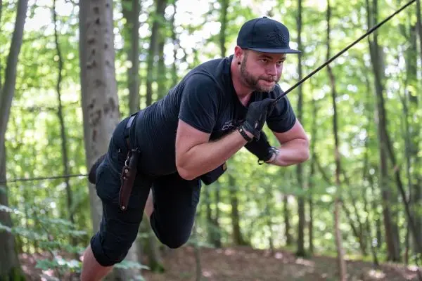 Mann nutzt Seil für eine selbstgebaute Seilbrücke im Wald