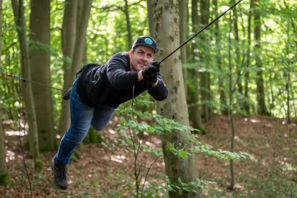 Mann schwingt an einem Seil zwischen Bäumen im Wald