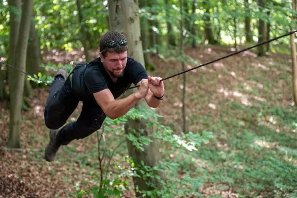 Mann schwingt an einer Seilbrücke zwischen Bäumen hindurch