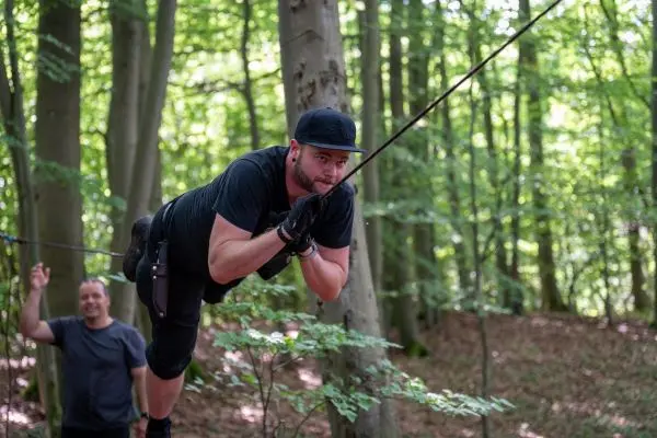 Mann schwingt an einer Seilbrücke zwischen Bäumen im Wald