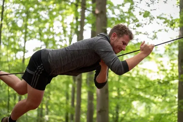 Mann zieht sich an einem Seil durch den Wald